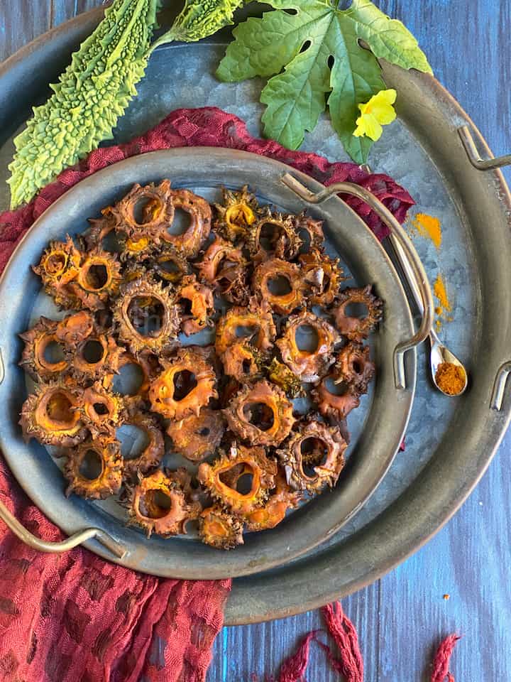 overhead shot of karela chips served in a rustic serveware stacked up with some spices on the side
