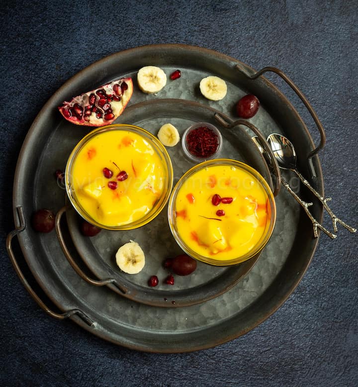 overhead shot of fruit custard served in two bowls with fruits on the side