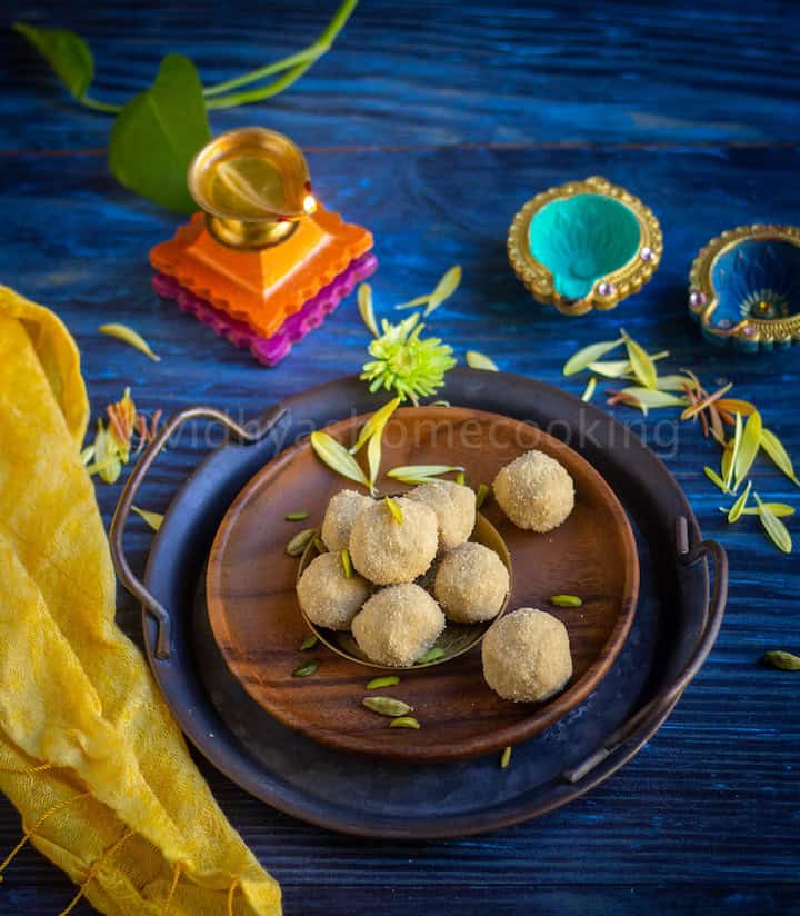 thinai laddu served on a wooden plate with flowers and nuts drizzled with lamps on the side