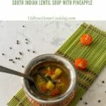 pineapple rasam in a traditional brassware placed on a green mat with tomatoes on the side with text overlay for pinterest