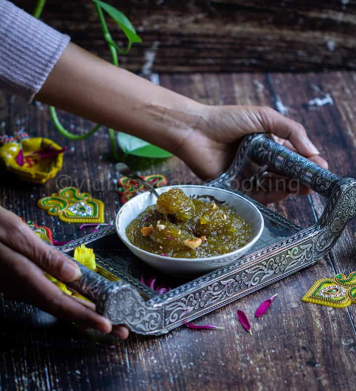 handshot depecting someone serving zucchini halwa in a bowl placed on the silver tray