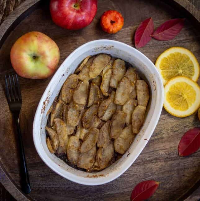 square image of brown betty in the french white baking dish with apples and lemon slices on the side