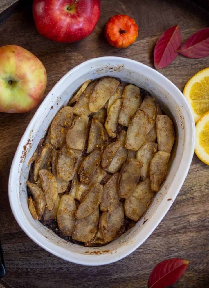 square image of brown betty in the french white baking dish with apples and lemon slices on the side