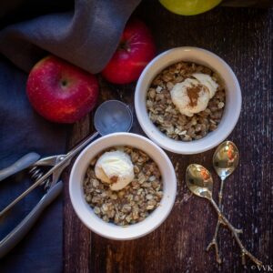 square image of apple crisp served with ice cream in a ceramic bowls