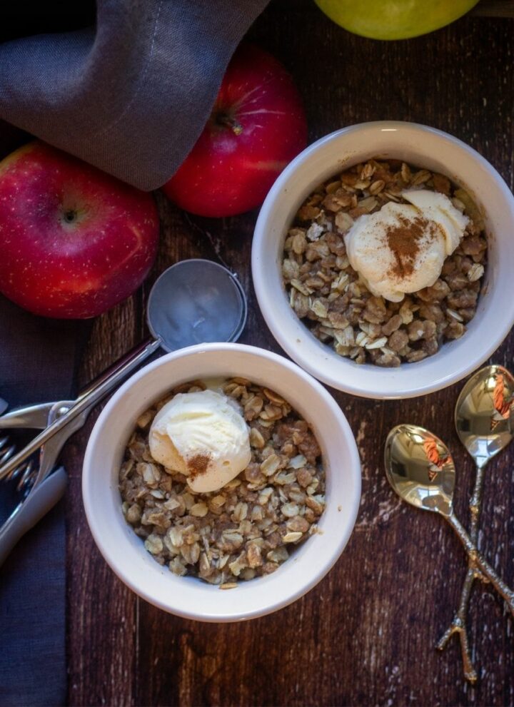 square image of apple crisp served with ice cream in a ceramic bowls