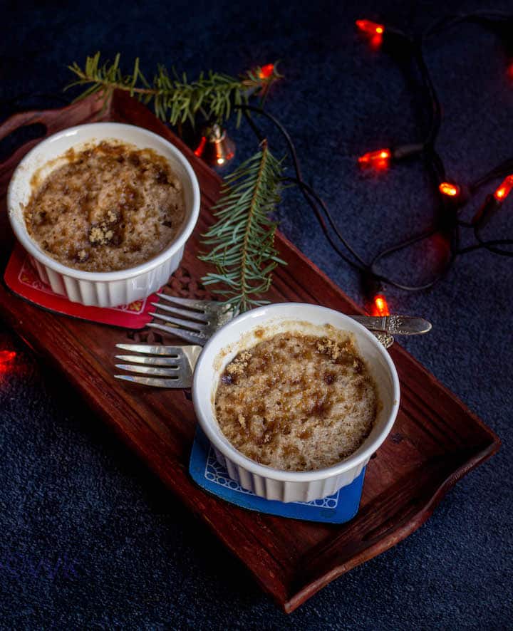 eggless coffee cake served in two ramekins placed on a wooden plate with lights and xmas leaves on the side