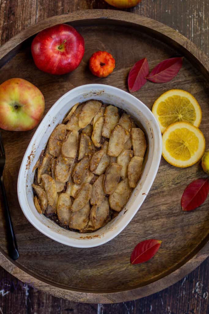 overhead shot of apple brown betty placed on a wooden board with some apples and lemon slices on the side