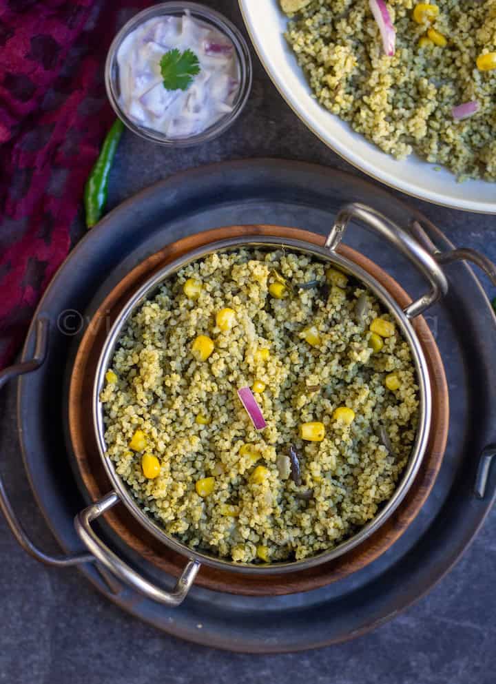 overhead shot of spinach rice served in a kadai stacked on plates with raita on the side