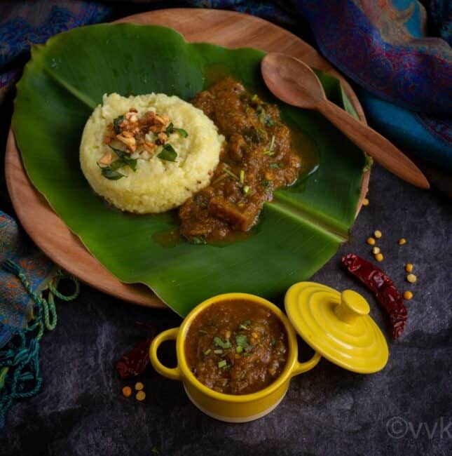square image of brinjal gothsu served in yellow casserole and plate of pongal and gothsu on the back