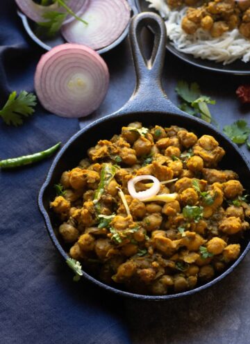 square image of pindi chole served in cast iron skillet with onions on the side