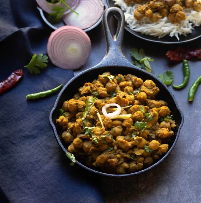 square image of pindi chole served in cast iron skillet with onions on the side