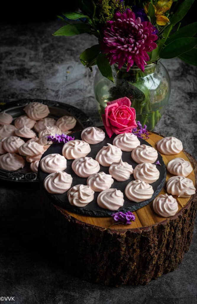 meringue cookies placed on a wooden stand with a flower vase behind