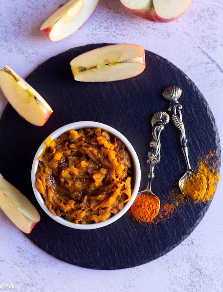 overhead shot of apple pickle with apple slices on the side and with some red chili and turmeric powder sprinkled