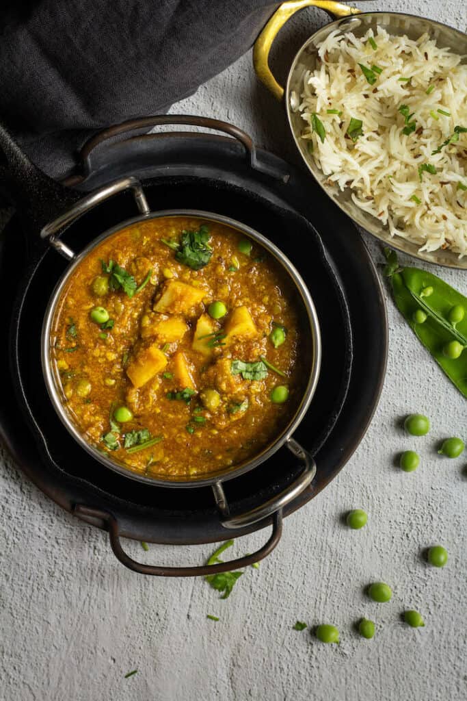 matar nimona served in a kadai bowl stacked up on trays with rice on the side and green peas on the other side