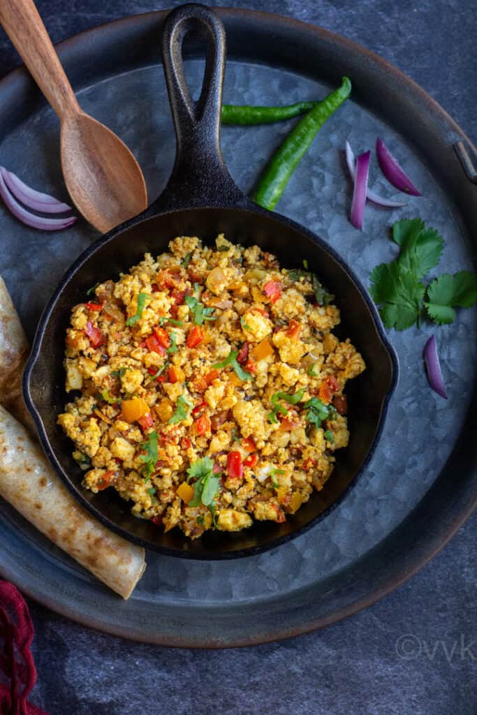 overhead shot of paneer bhurji served in cast iron pan placed on rustic tray with roti on the side