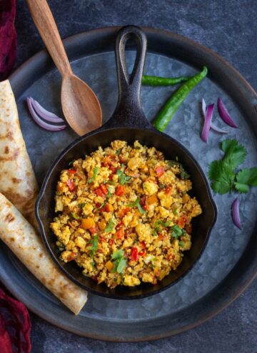 overhead shot of paneer bhurji served in cast iron pan placed on rustic tray with roti on the side