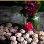 vegan meringue cookies placed on a wooden stand with a flower vase behind with text overlay for pinterest