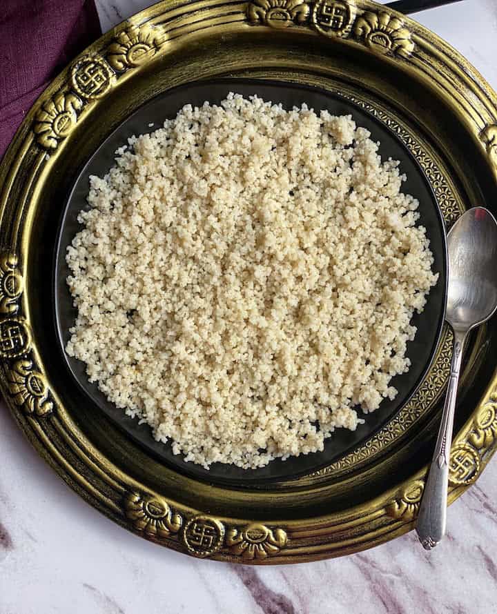 overhead shot of barnyard millet placed in black plate on top of golden plate with purple fabric on the side