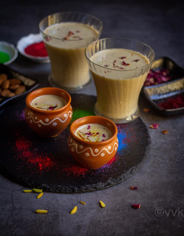 thandai served in kulhad cups and glass cup placed on a black board with colors