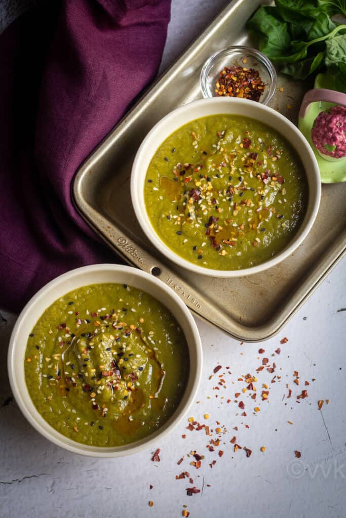 creamy asparagus soup seved in two bowls with maroon fabric on the side