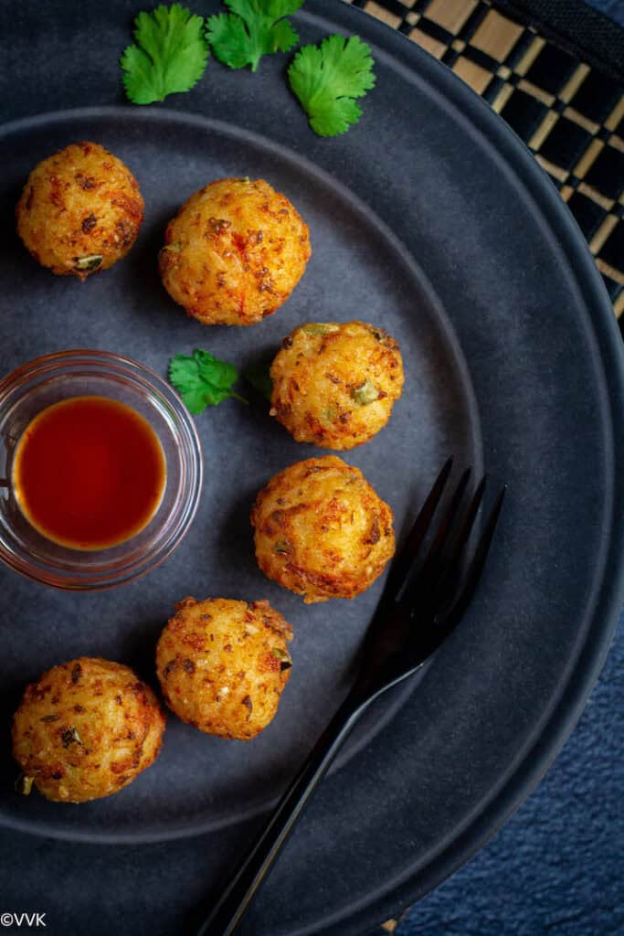 overhead shot of rice veggie and cheese balls served in a blue tray with tomato sauce in the middle