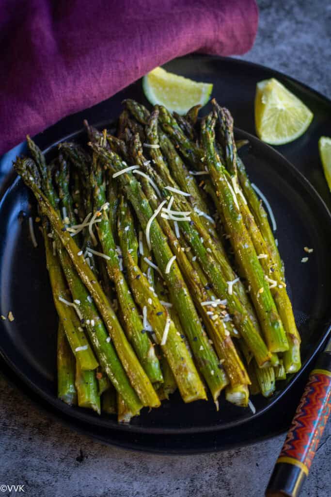 overhead shot of oven-roasted asparagus served on a black plate with lemon wedges on the side