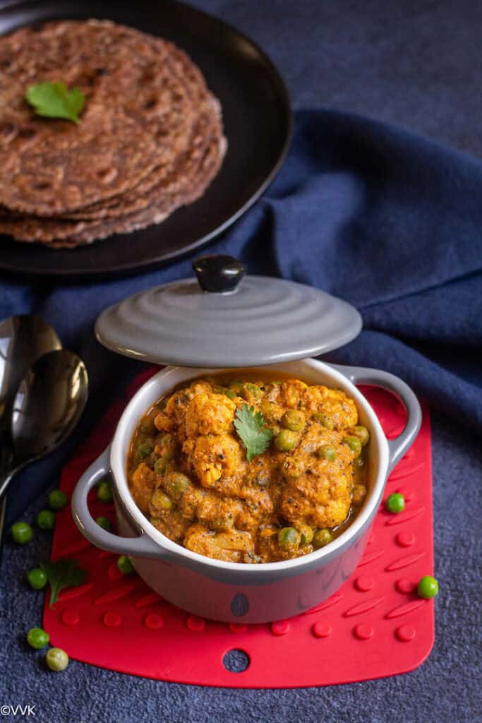 gobi matar served in a gray casserole placed on a red coaster with ragi rotis on the top