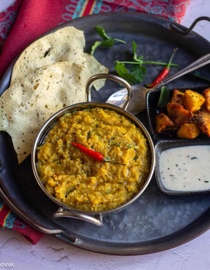 arisi paruppu sadam served in kadai with papad, raita and arbi roast placed on a rustric tray