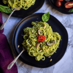 square image of pesto pasta served in black plate with cherry tomato on top