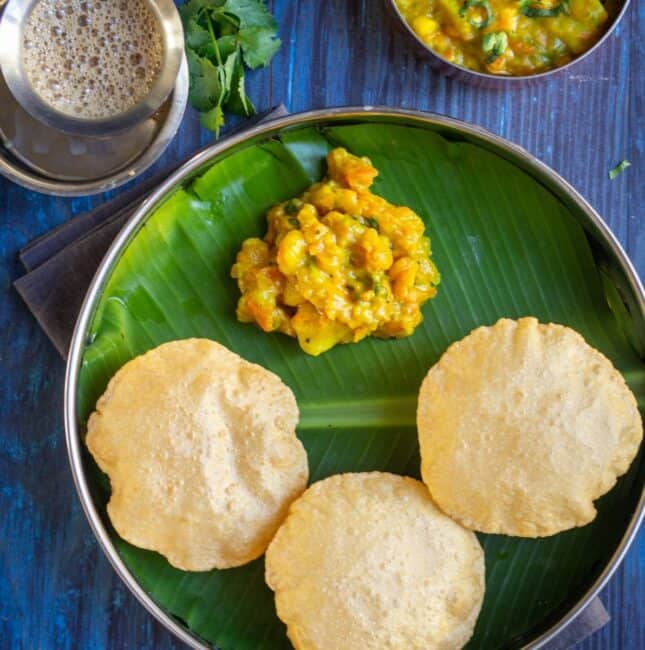 poori served with potato masala in a plate lined with banana leaf and coffee on the side