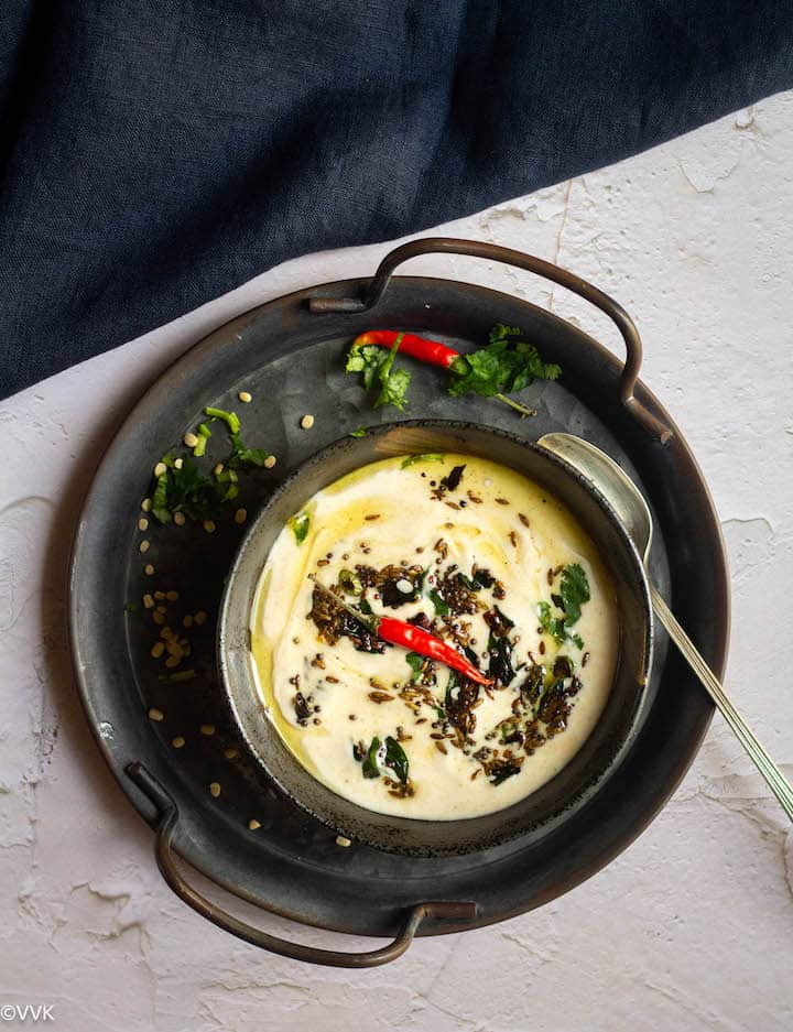 Uradl dal flour raita served in black bowl placed on a iron tray with a spoon on the side