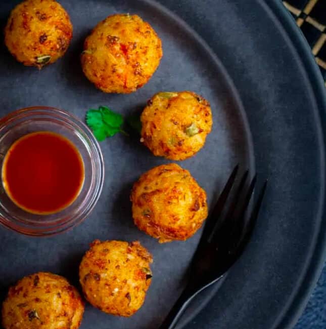 Rice Cheese and Veggie Balls served in a shape of a circle with a mini bowl of sauce in the center of the plate