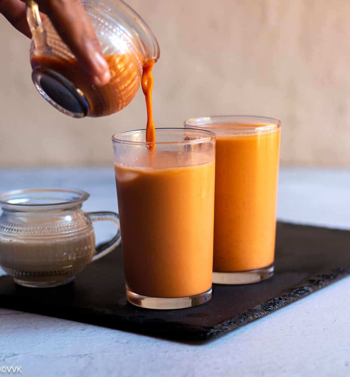 pouring shot of thai iced tea into a tall glass placed on slate board