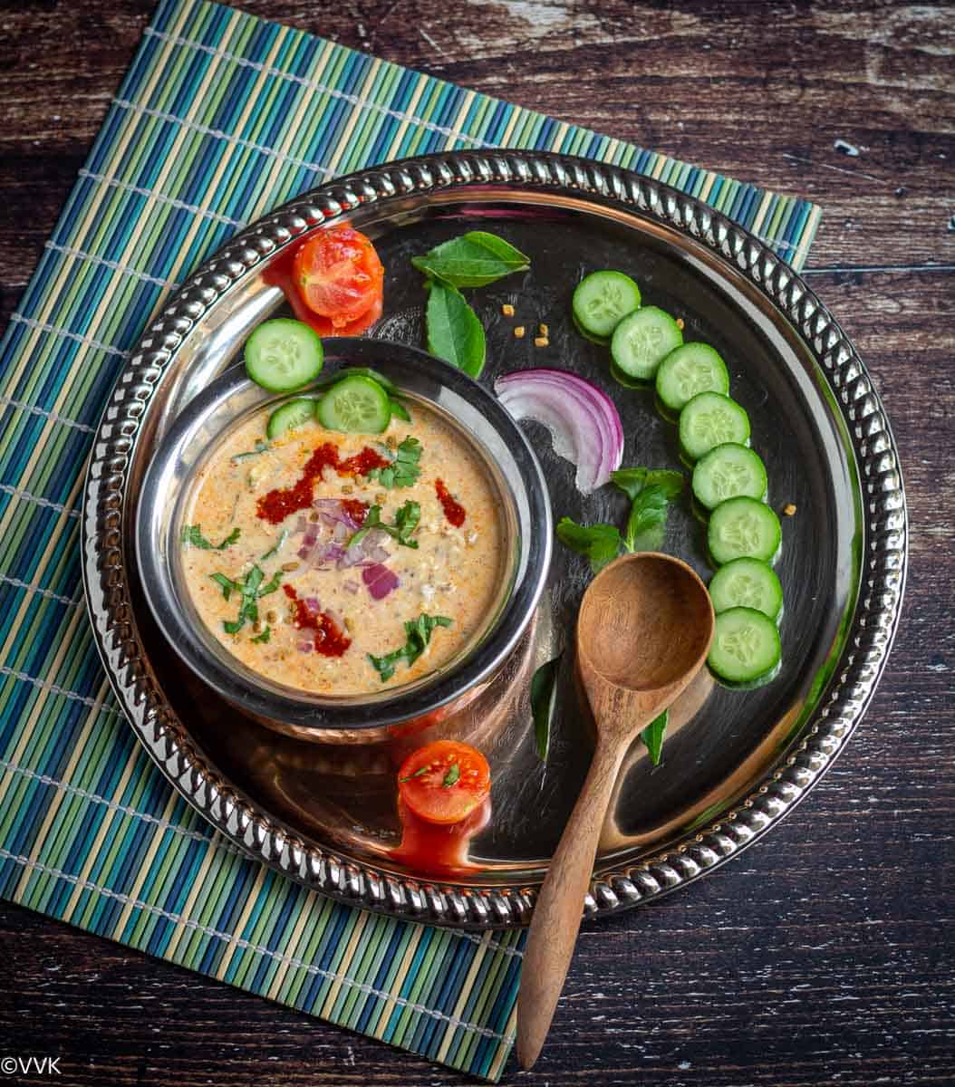 Overnight oats served in kadai placed on a plate with wooden spoon and freshly cut cucumbers.