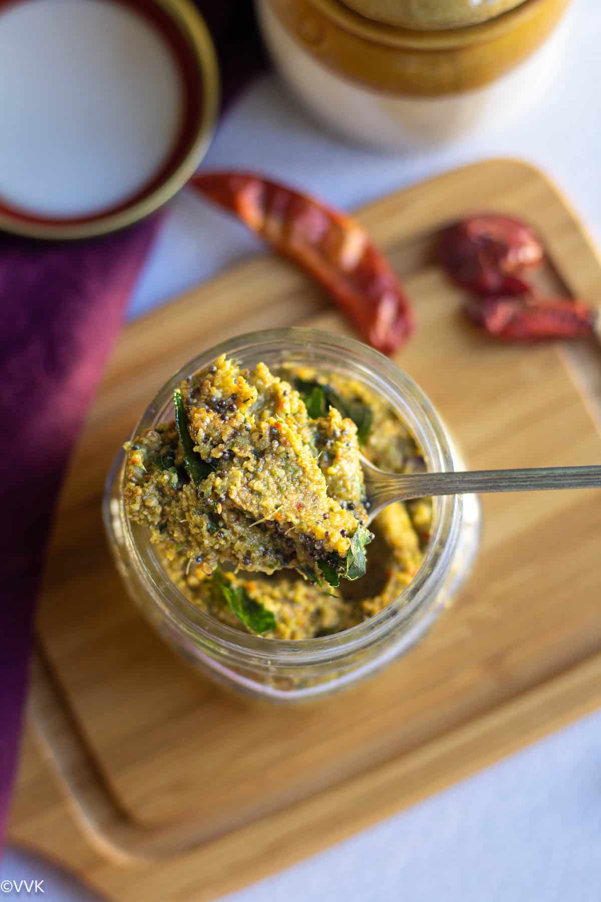 overhead shot of pperkangai thuvaiyal in a glass jar with spoonful of chutney