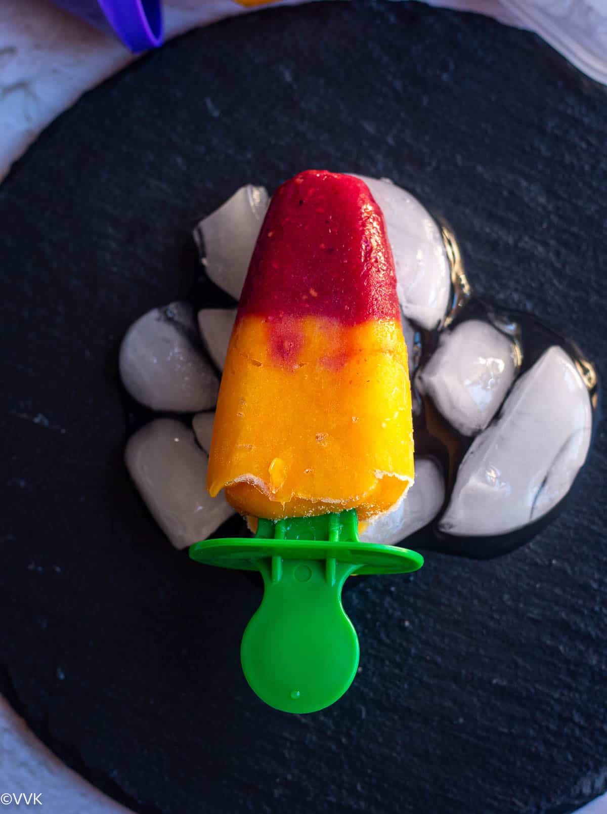 mango raspberry popsicles placed on black plate with ice cubes 