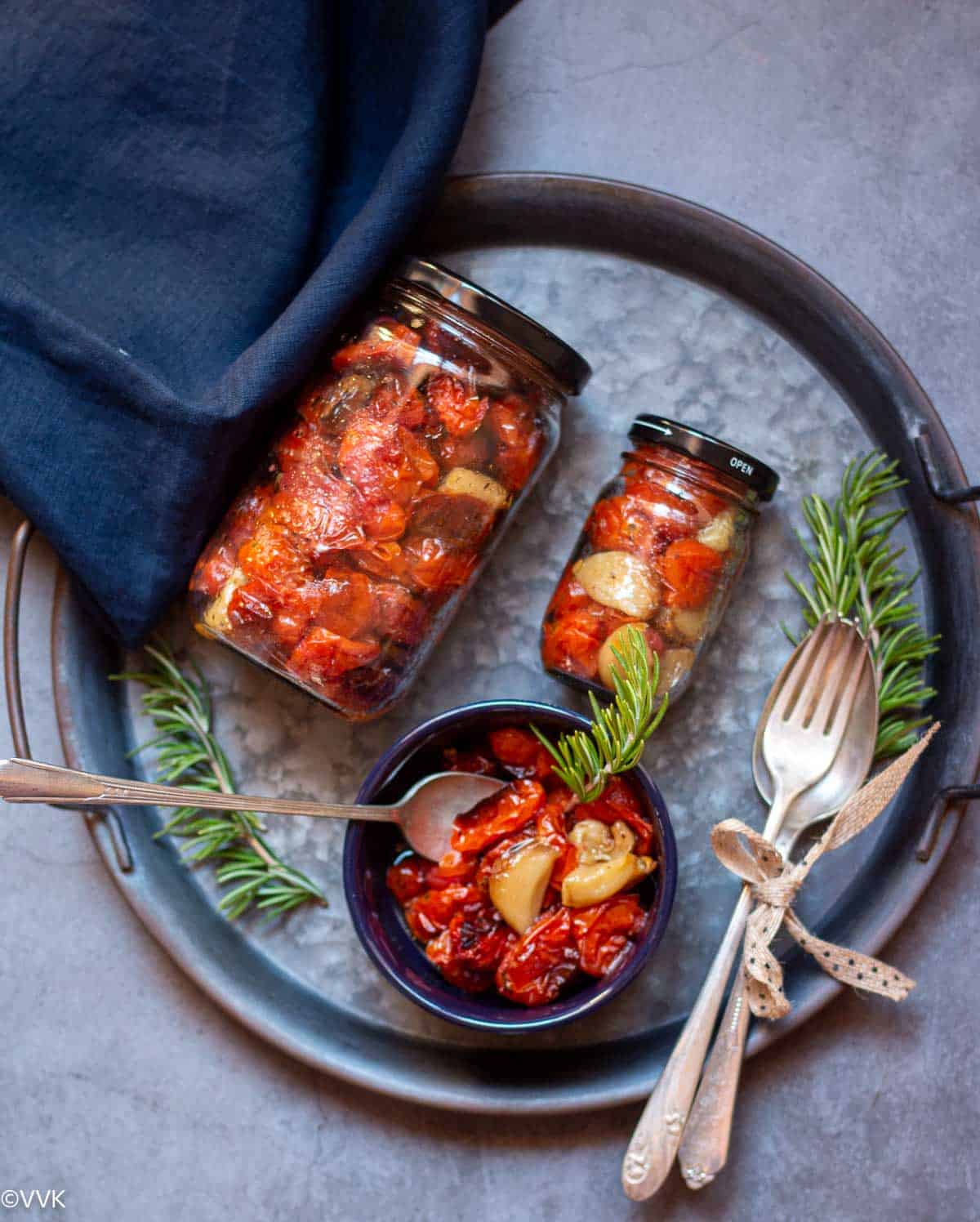 roasted tomatoes stored in jars and placed in black bowl on a iron tray with rosemary sprigs on the side