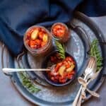 square image of roasted tomatoes in jars and black bowl