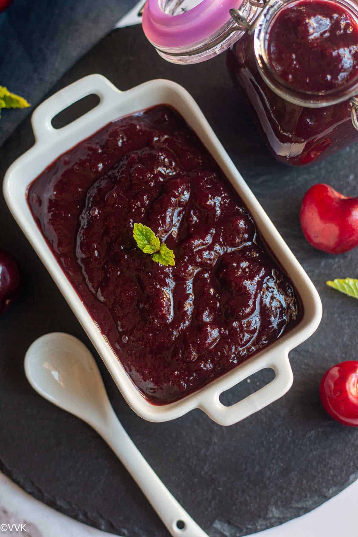 overhead closeup shot of cherry relish served in white serveware placed on black slate board