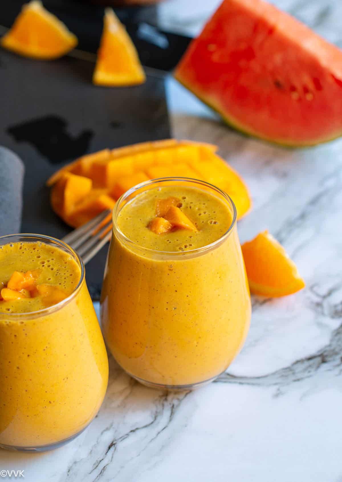 mango smoothie topped with mangoes with some fruits on the side placed on a black slate board