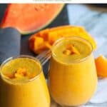 vegan mango smoothie served in two glasses topped with mangoes with text overlay for pinterest