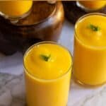 close up shot of tropical mango smoothie served in two glasses with text overlay for pinterest