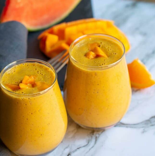 square image of mango breakfast smoothie served in two glasses with some watermelons