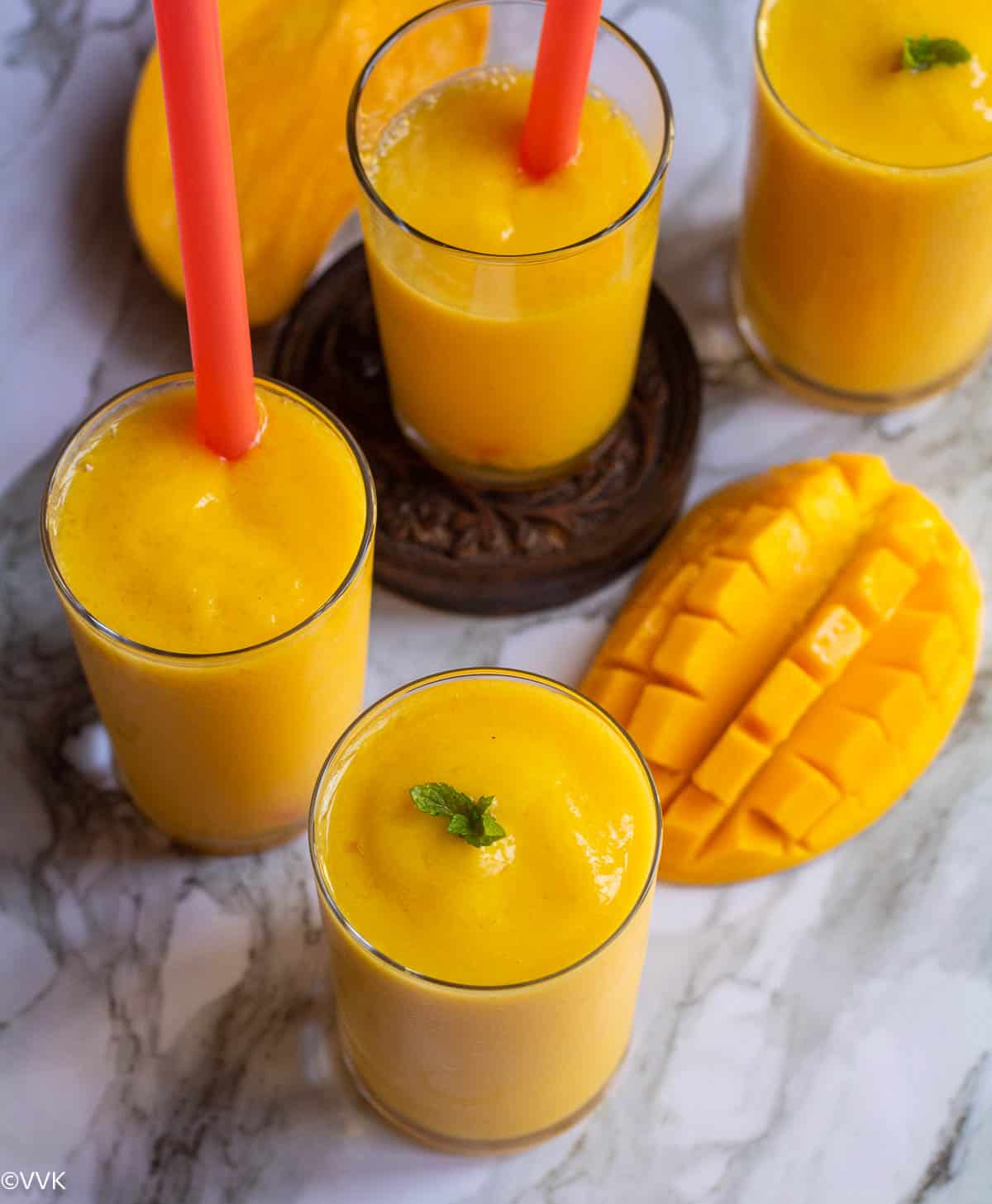 tropical smoothie served in four glasses with straw in one glass with cut mango on the side