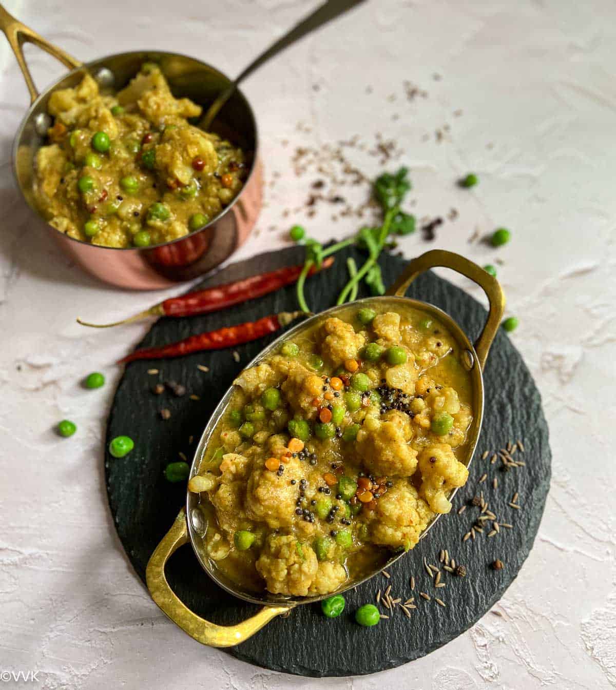 cauliflower kootu placed on a black slate board with cilantro and red chilies on the side and one more bowl of kootu on the top