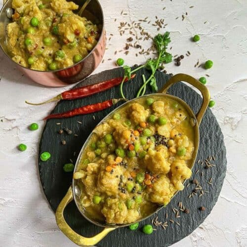 square image of cauliflower kootu placed on a black slate board with cilantro and red chilies on the side