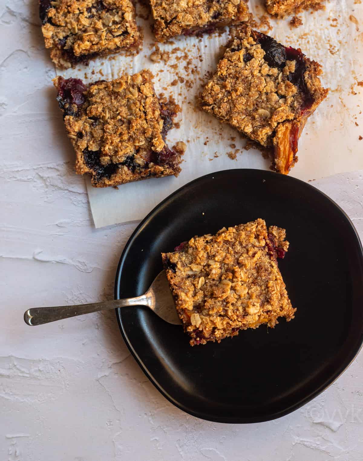 cherry mango crumb bars placed on a black plate on top a fork with few other bars behind