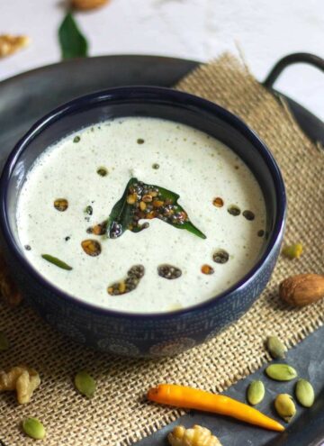 square image of nuts coconut chutney served in blue serveware placed on burlap cloth on a tray with nuts and chilies on the side