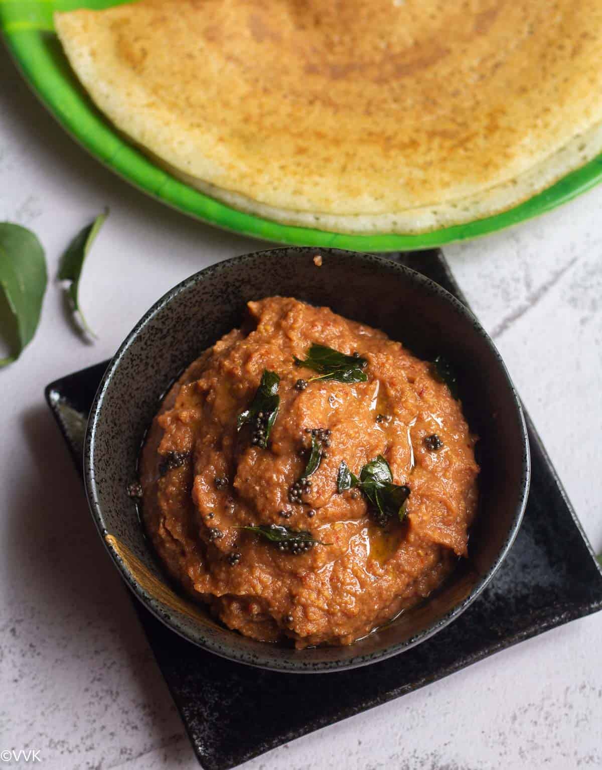 overhead closeup shot of onion chutney topped with tempering with dosa behind