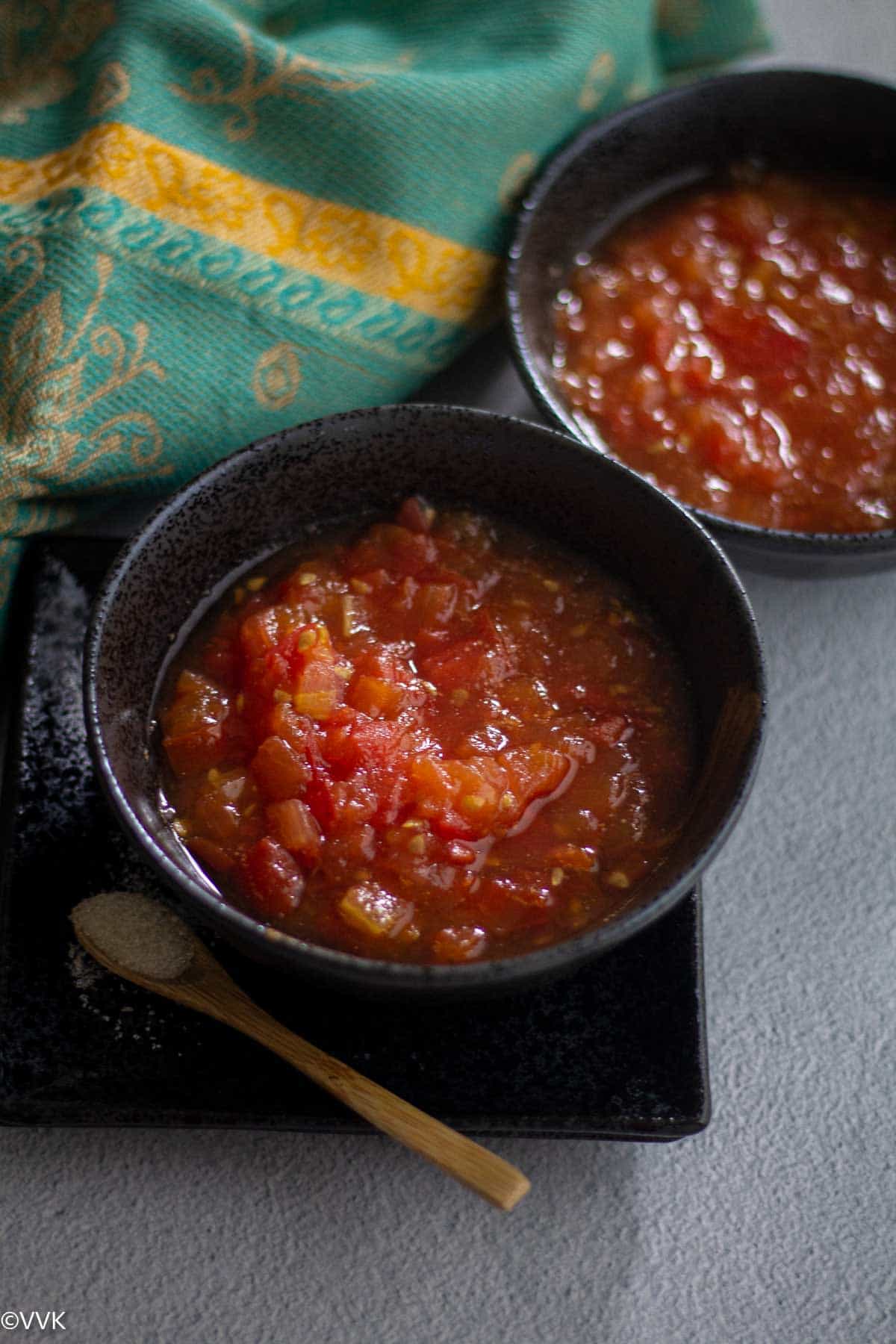 close up shot of tomato sweet pachadi served in black bowl with wooden spoon with sugar